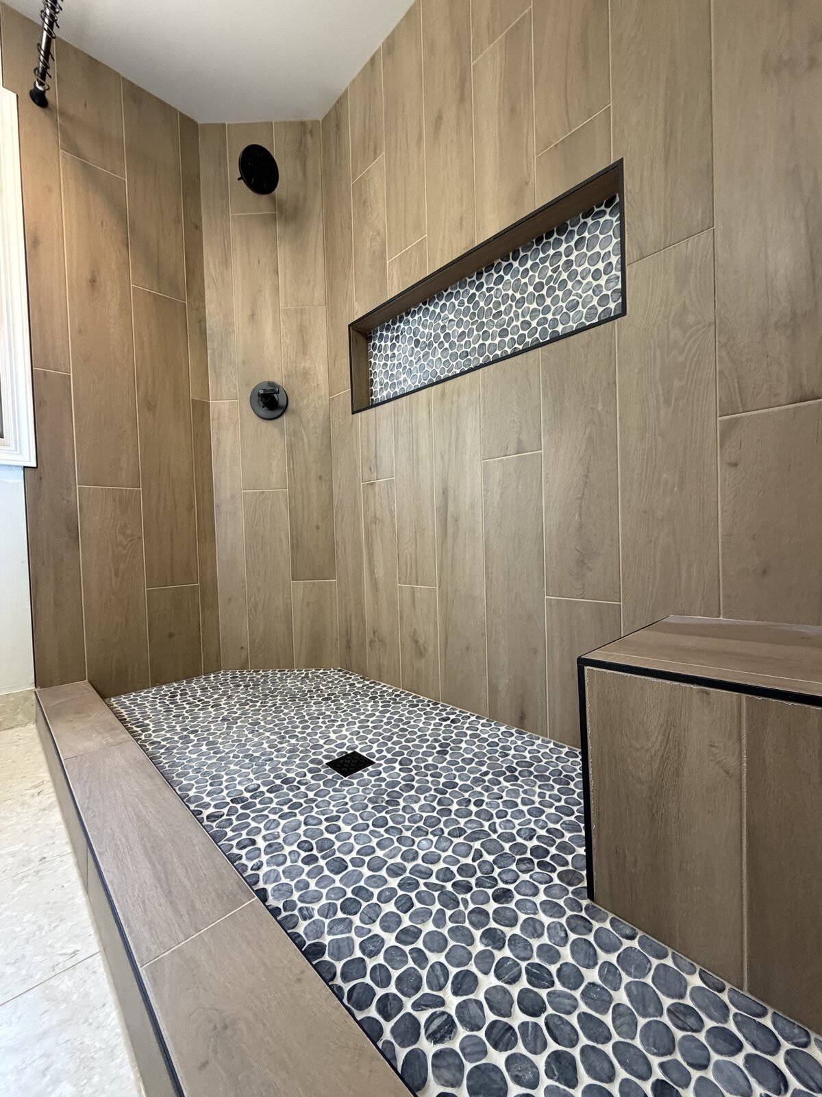 Custom shower with wood-look tile walls and pebble mosaic floor